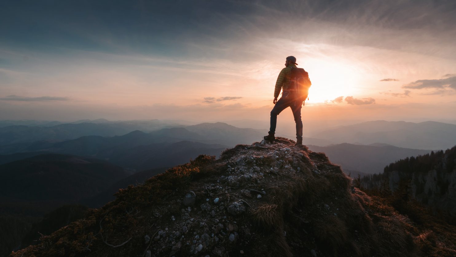 Man at the top of the mountain representing self-improvement and emotional wellbeing Man on top of mountain at sunrise representing self-improvement and emotional well-being.
